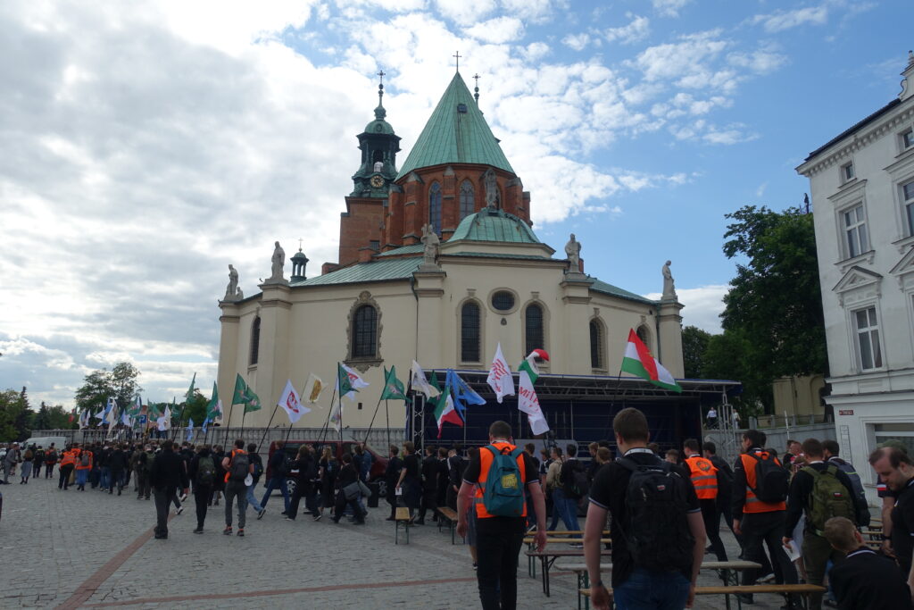 Grupa pielgrzymów Pielgrzymki Kościoła Walczącego gromadzi się przed Bazyliką Prymasowską w Gnieźnie, obok ołtarza polowego.