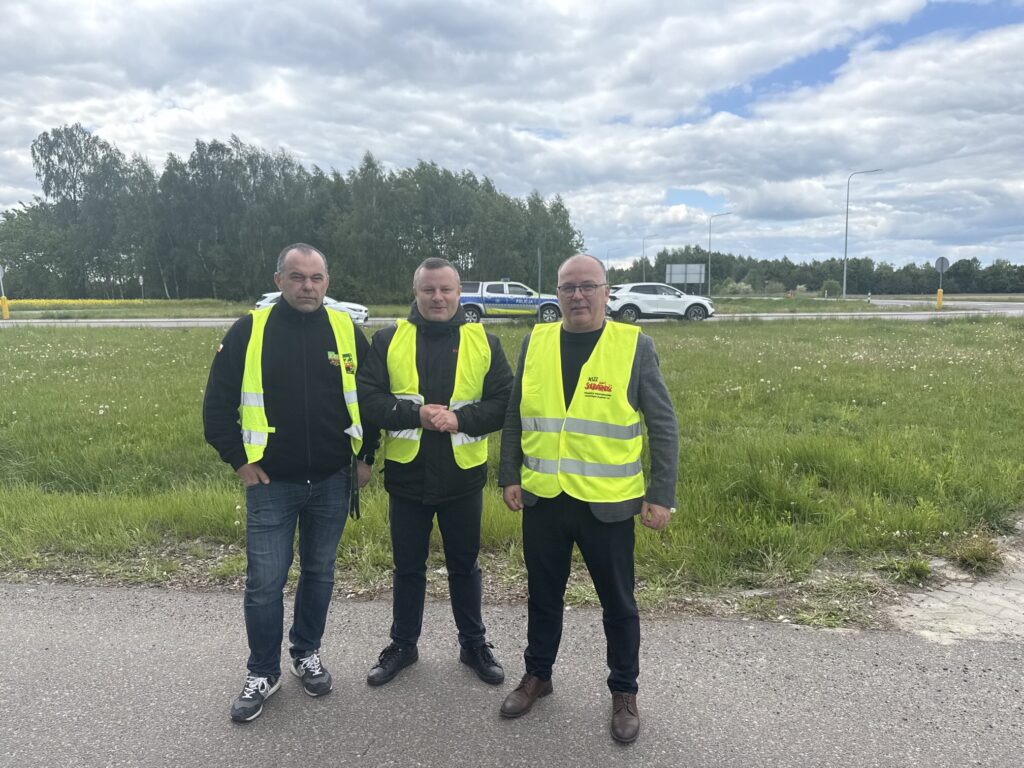 Rafał Mekler i organizatorzy protestu przewoźników w żółtych kamizelkach na tle drogi krajowej nr 12 w Dorohusku.